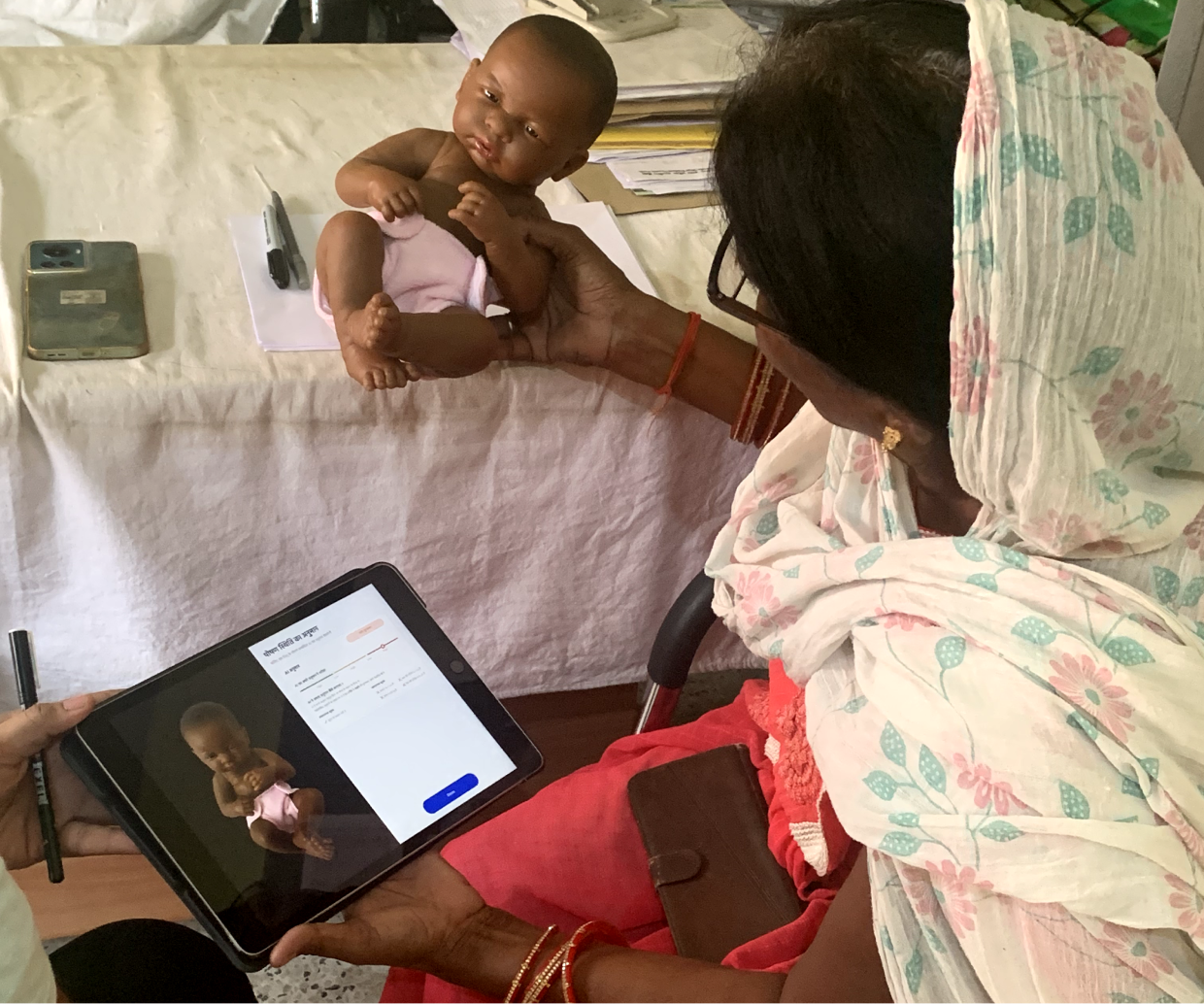 A picture of a community health worker in an interview comparing a doll to an iPad AI decision.
